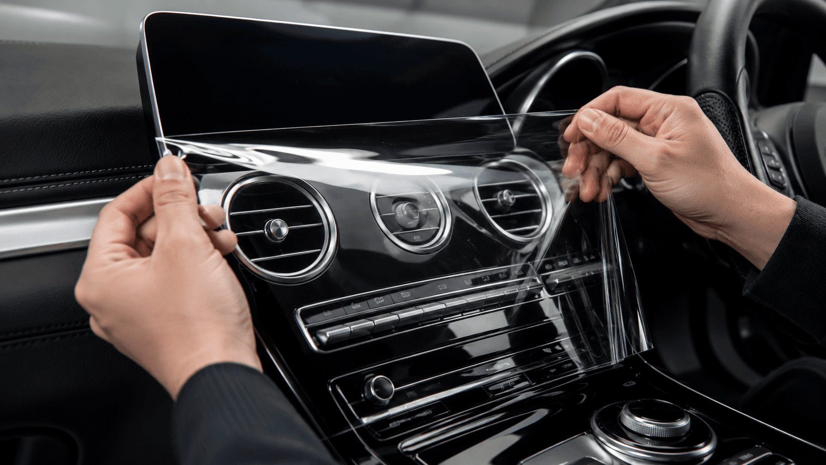 Hand applying pre-cut interior PPF to a glossy centre console and AC vents